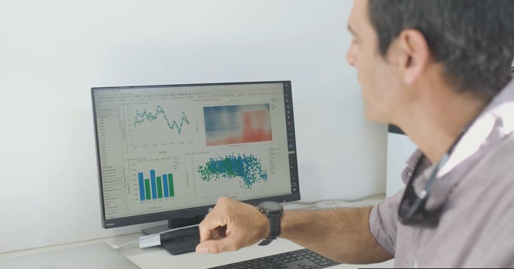 Man looking at computer screen with graphs and charts on it.