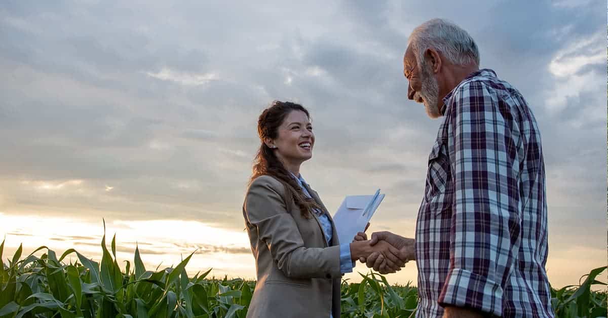 A man and a woman in a field shaking hands.
