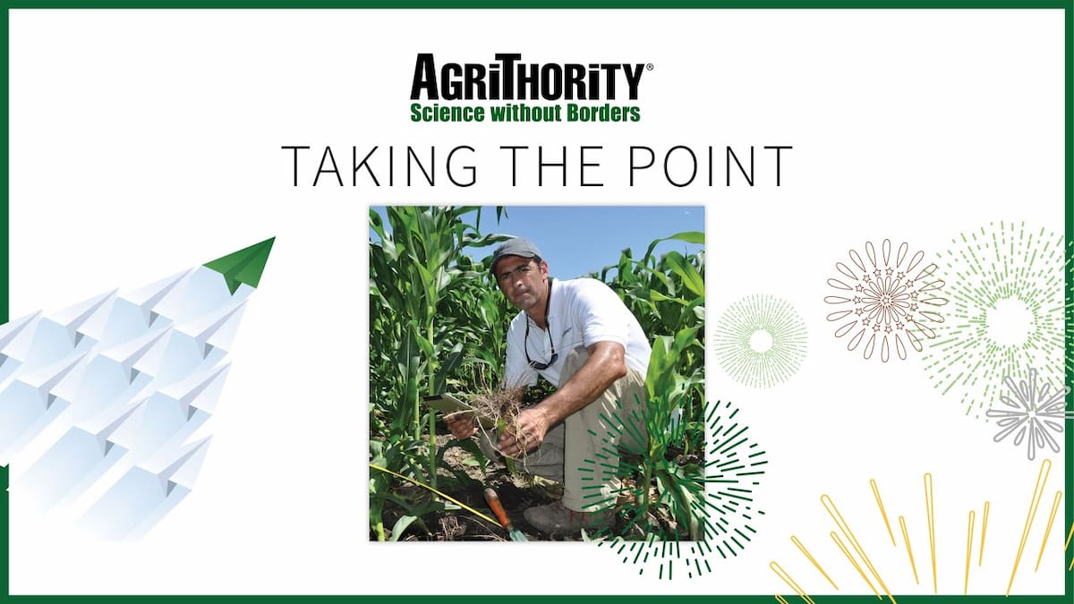 A promotional image for AgriThority® with the text "TAKING THE POINT" and the tagline "Science without Borders." It features a photo of Ignacio Colonna in a white shirt working in a cornfield, alongside illustrations of a green arrow with paper planes and decorative starburst patterns. The AgriThority® logo is at the top.