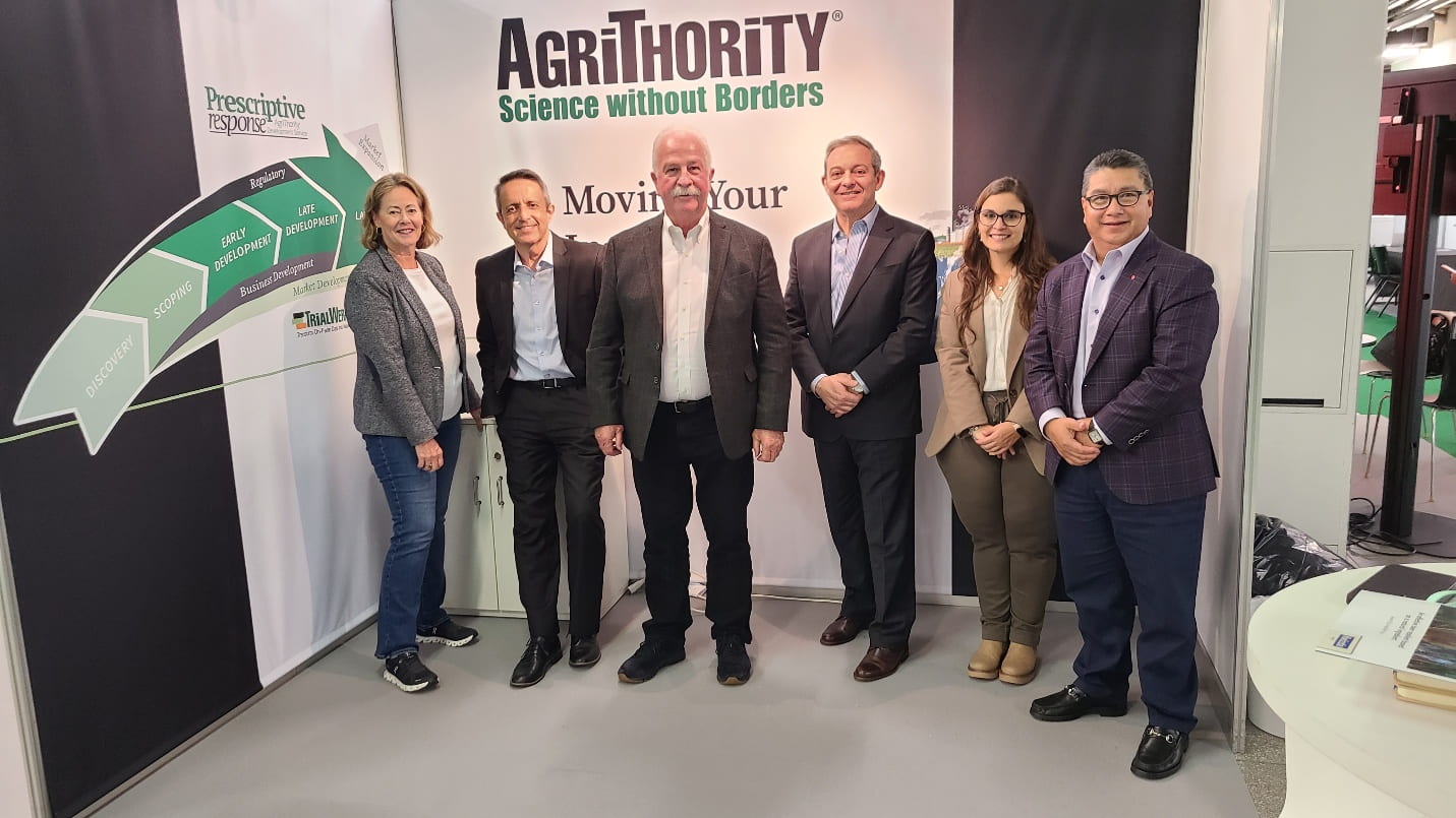 Six AgriThority® team members standing in front of the AgriThority® booth, showcasing "Science without Borders" and "Moving Your Innovation to Market" slogans, with a Prescriptive Response chart, highlighting agriculture innovation and business development solutions.